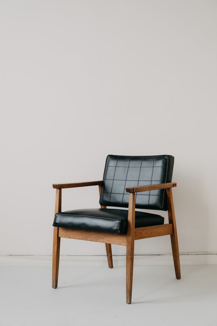 Classic mid-century modern armchair with black leather upholstery on minimalist backdrop, capturing retro style.